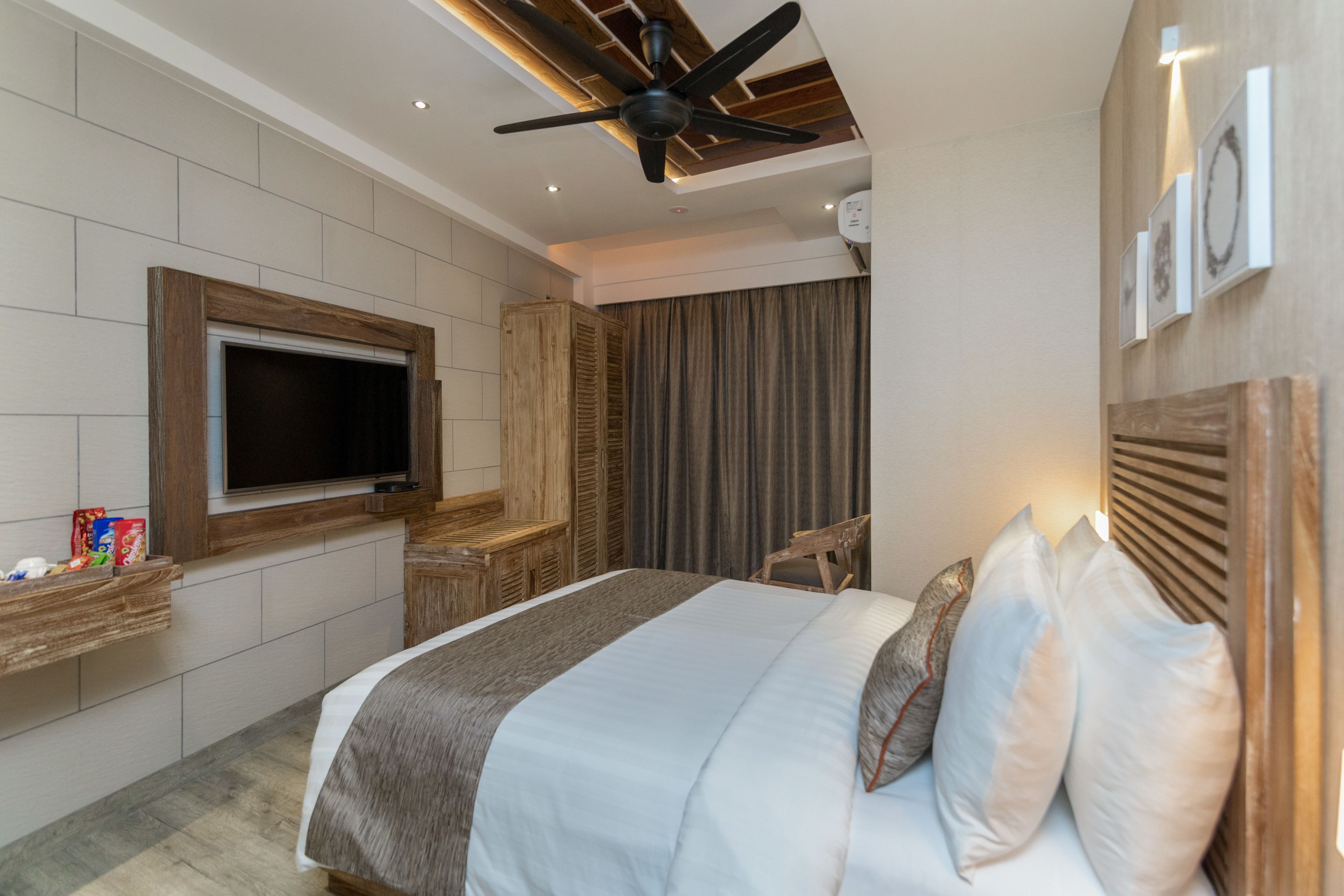 Une chambre d’hôtel moderne dotée d’un grand lit, d’un téléviseur à écran plat fixé au mur, d’une tête de lit en bois et d’un ventilateur de plafond.
