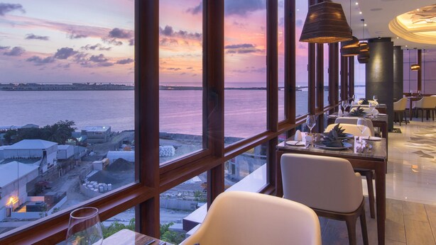 A restaurant with a view of the sea at sunset, featuring large windows, modern lighting, and a clean dining area.