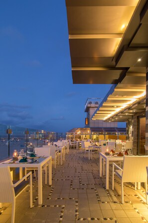 An outdoor dining area with tables and chairs, a clear sky, and a view of the cityscape.
