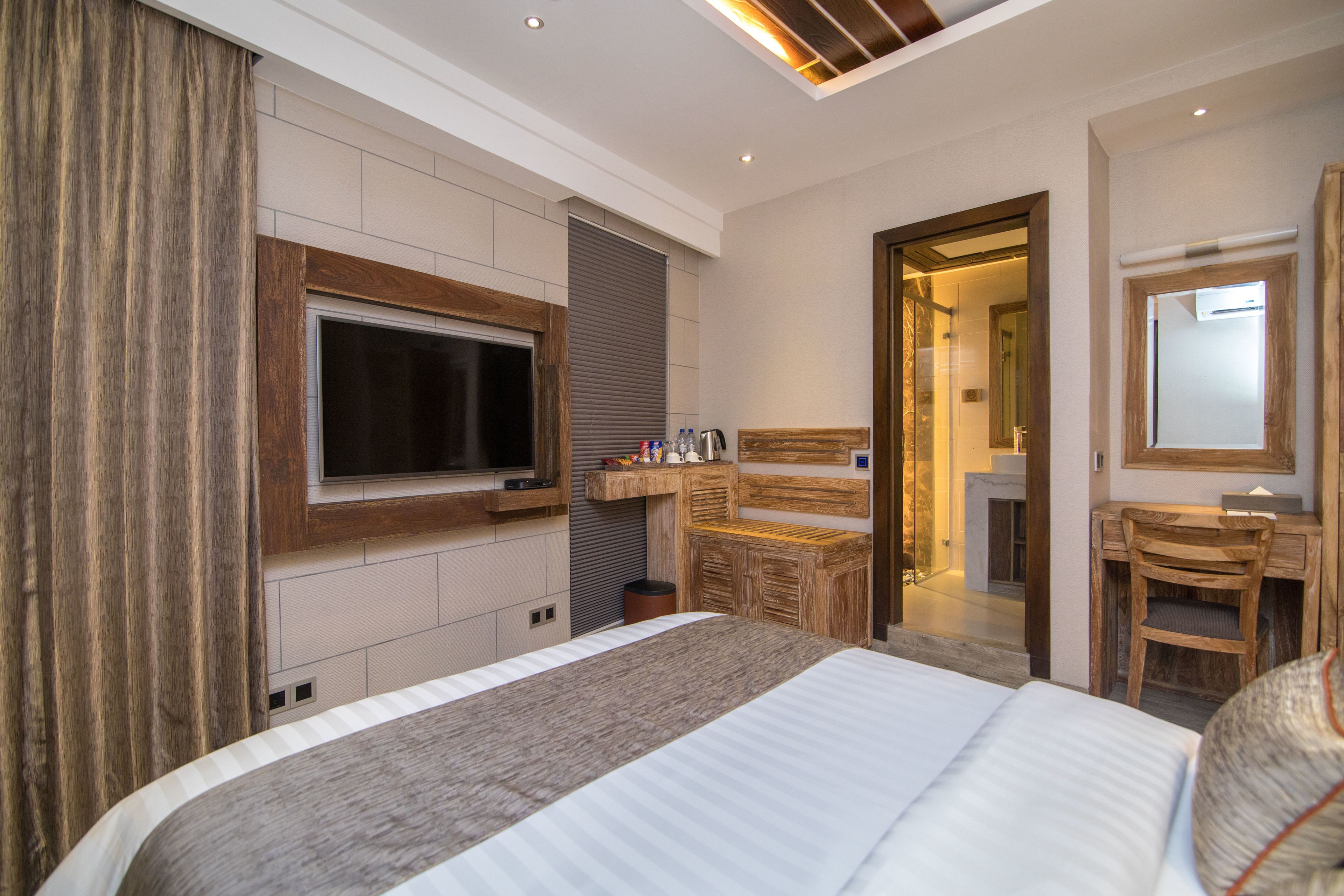 A modern hotel room with a large bed, a television mounted on the wall, a wooden desk, and a mirror.
