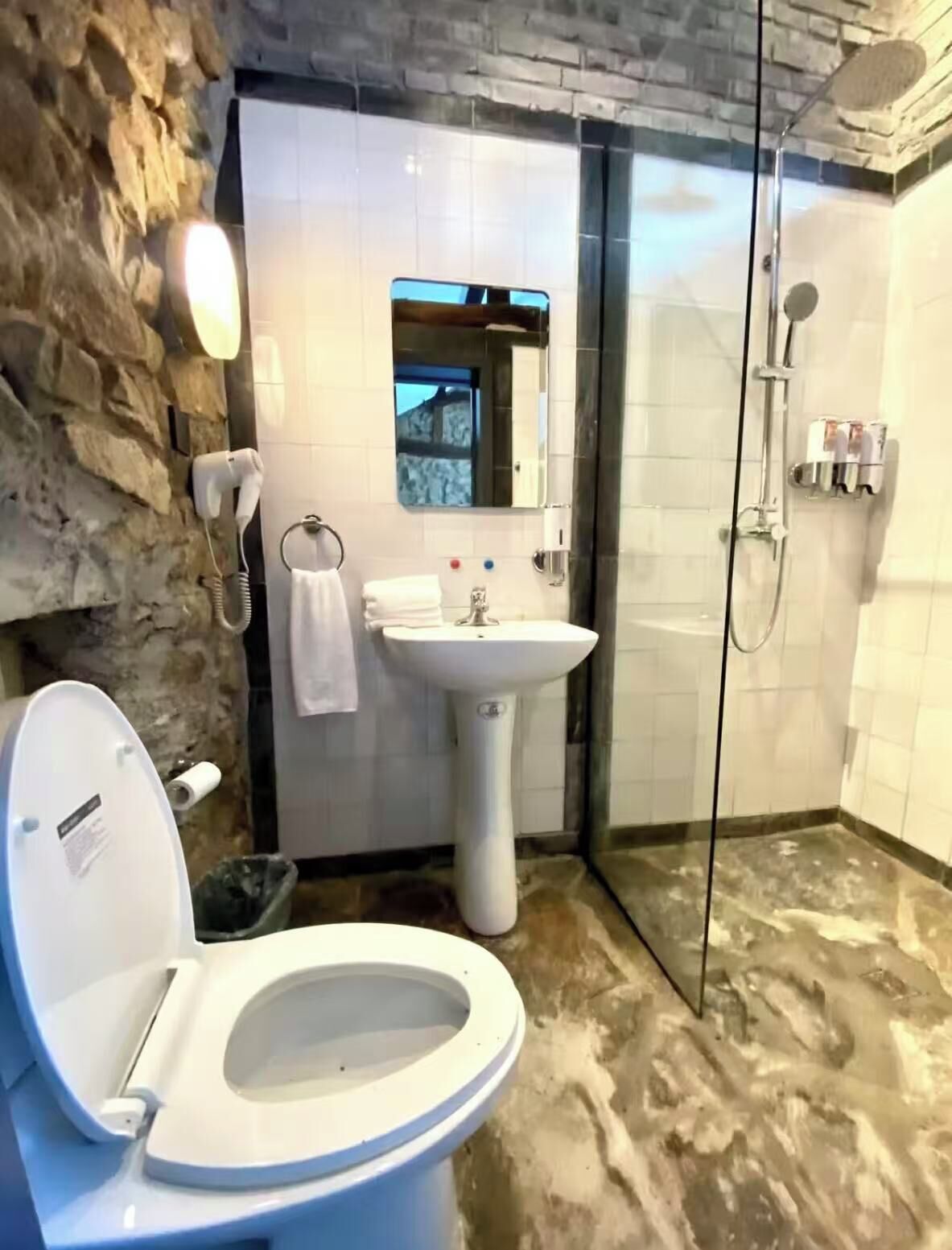 A bathroom with a stone wall, a white sink, a toilet, and a glass-enclosed shower area.