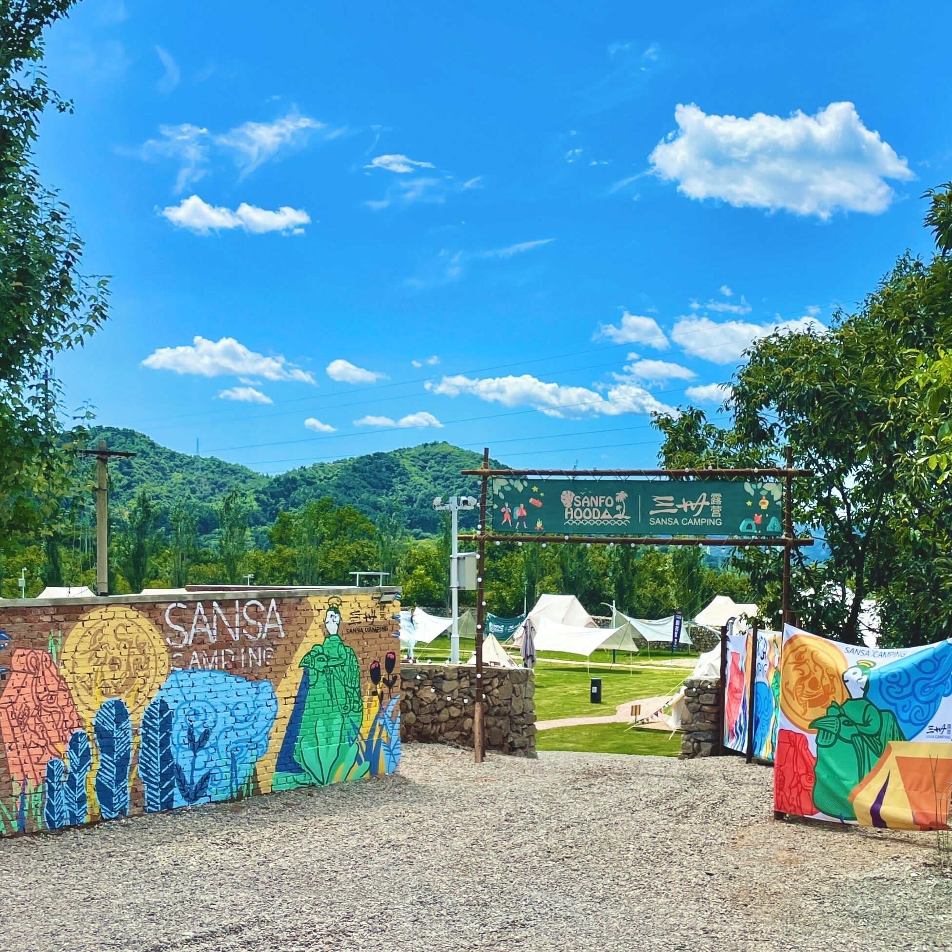 Entrada a un camping con un mural colorido, tiendas de campaña y un cielo azul despejado.