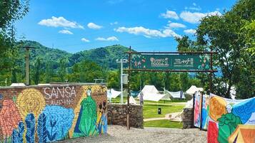Eingang eines Campingplatzes mit farbenfrohem Wandgemälde, Zelten und blauem Himmel.