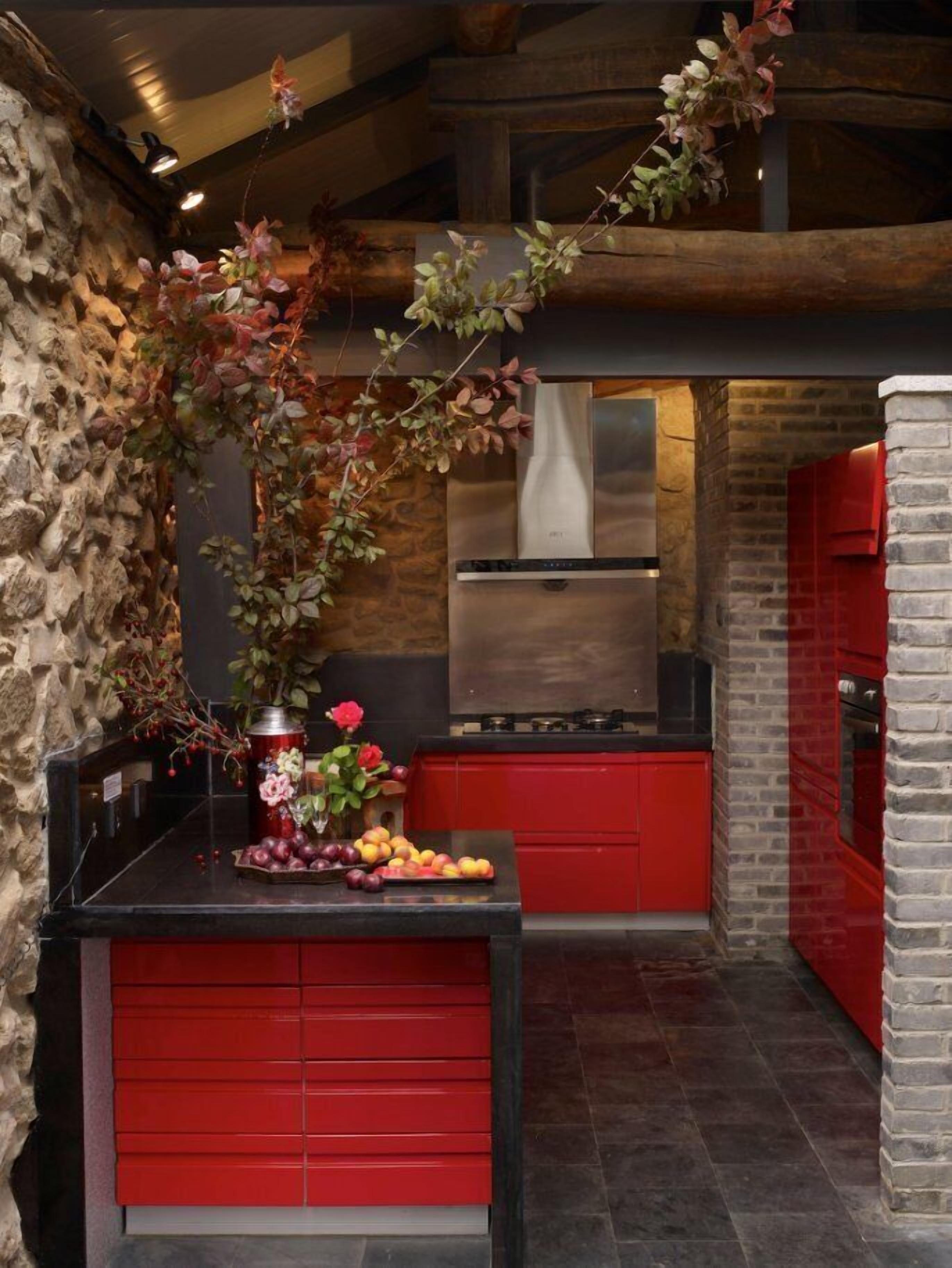 Una cocina con armarios rojos, una pared de piedra y una planta colgante.
