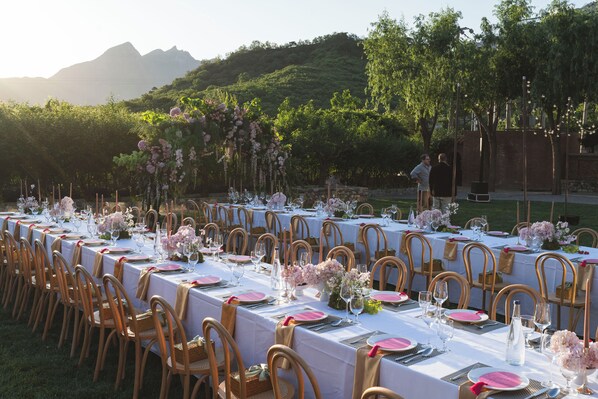 A long table set for a formal outdoor event with chairs and tables arranged in rows.