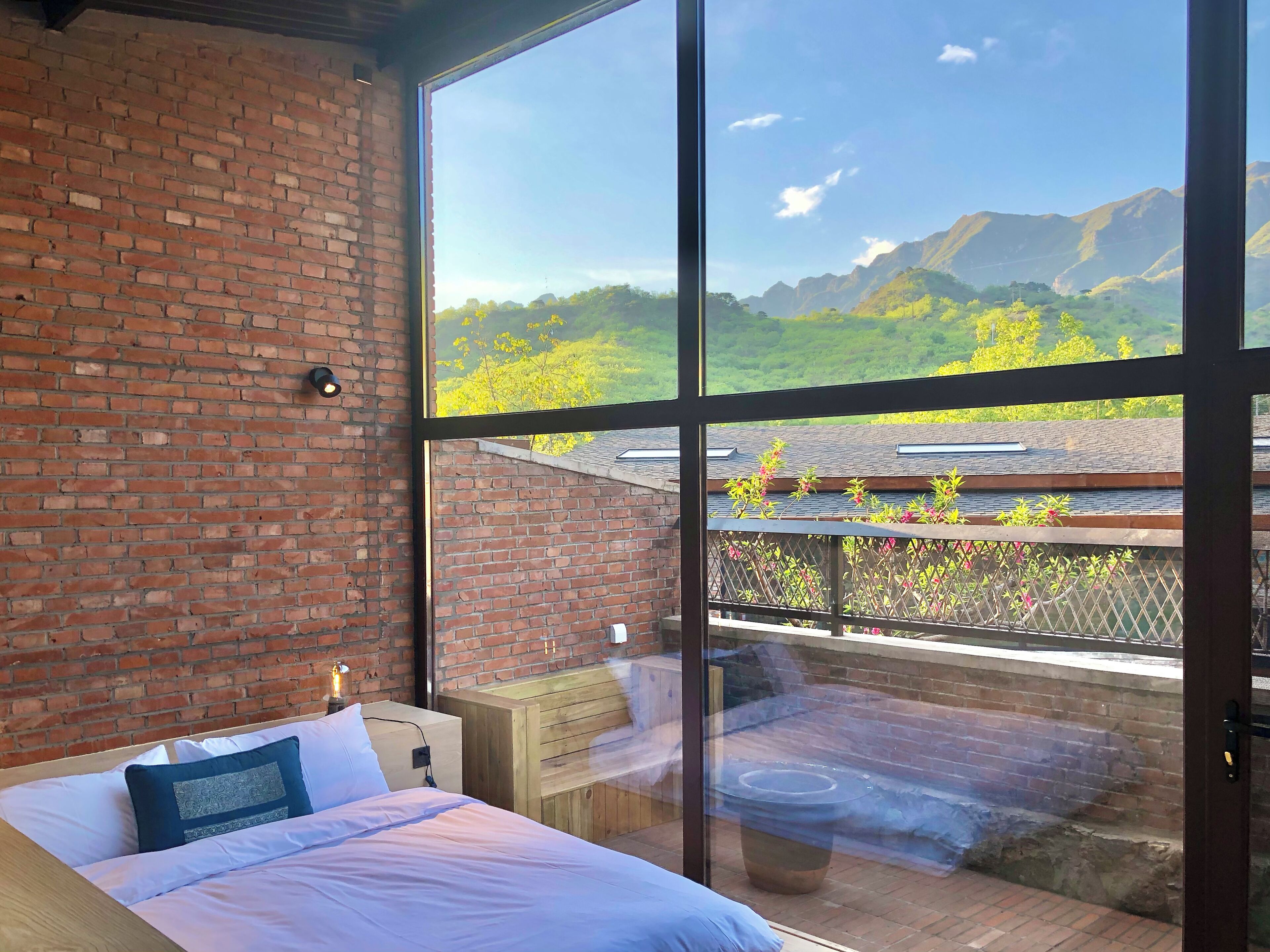 A bedroom with a large window, a brick wall, and a wooden bed.