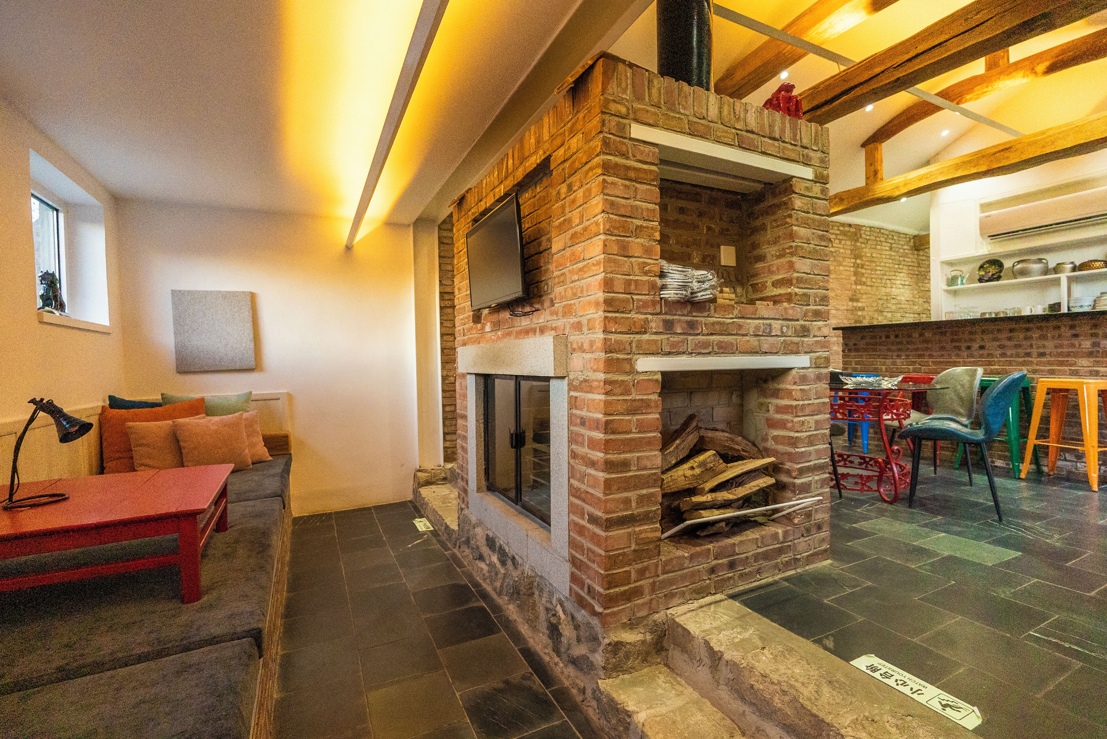 A cozy living area with a brick fireplace, a television mounted on the wall, and a comfortable seating area with a sofa and a red table.