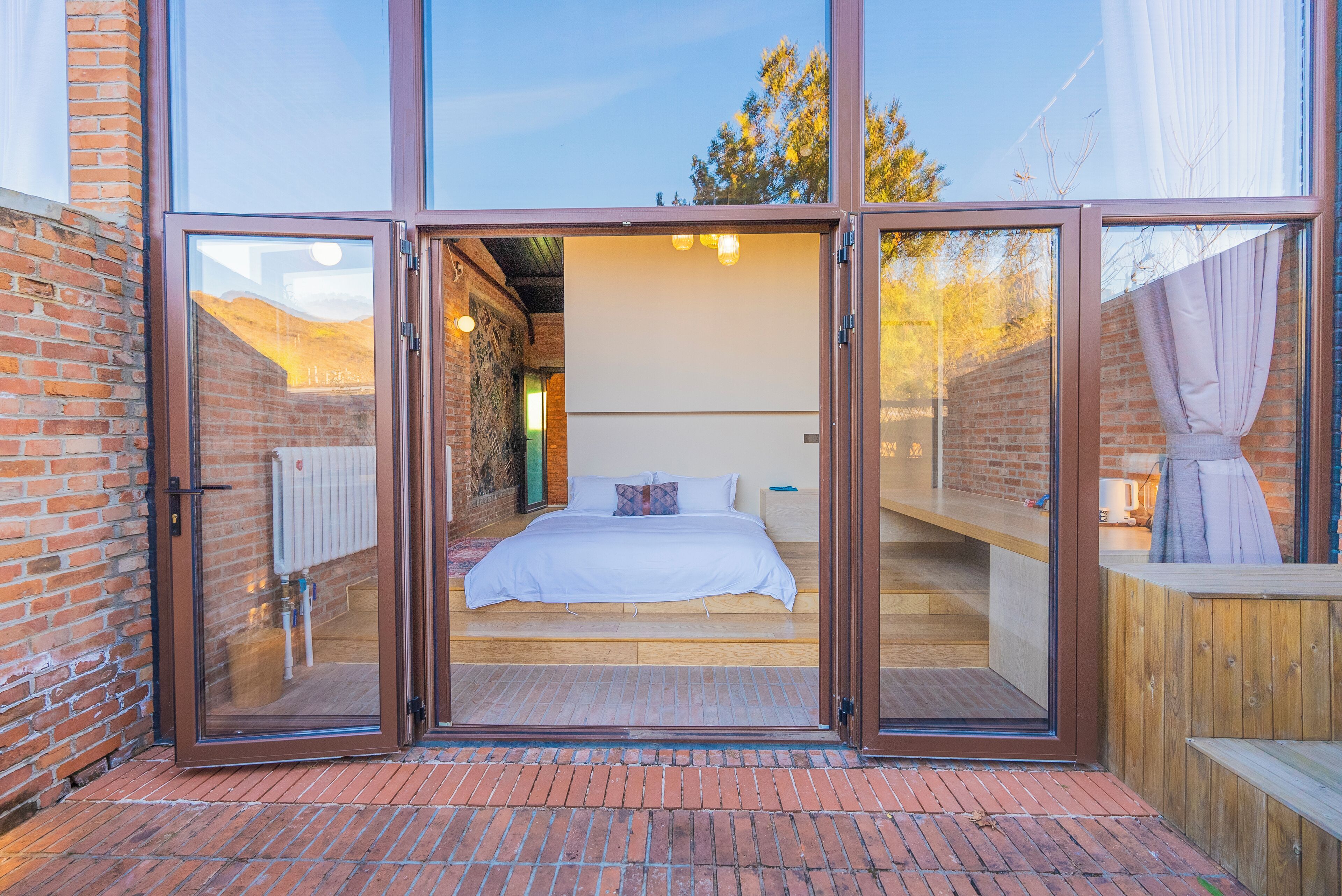 A bedroom with a large sliding glass door, a bed with white bedding, and a view of the outdoors.