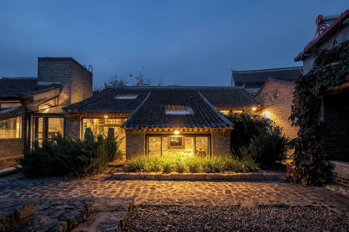 A traditional house with a tiled roof, a stone pathway, and a well-lit entrance.