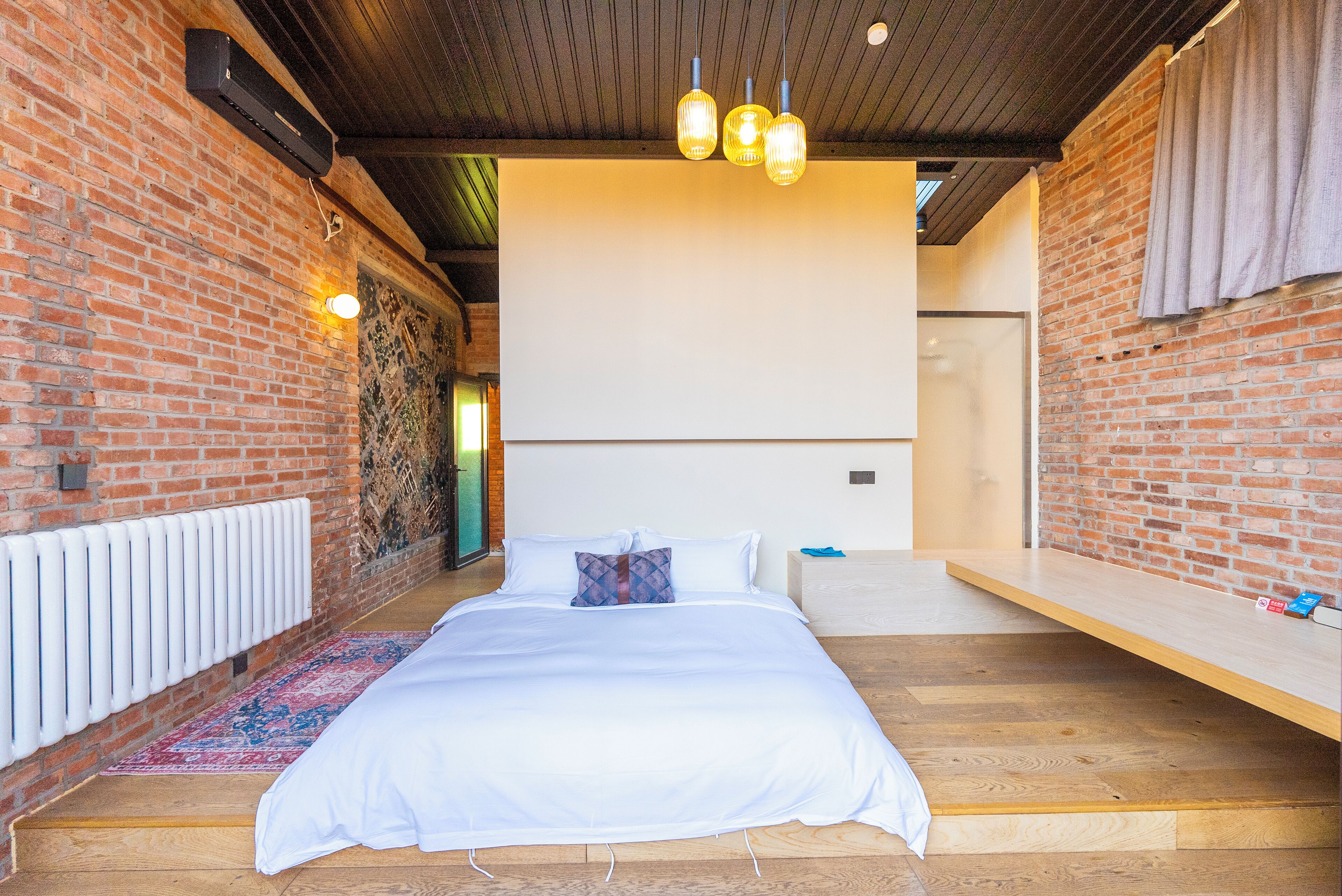 A bedroom with a large bed, a wooden floor, a brick wall, and a ceiling with exposed beams.