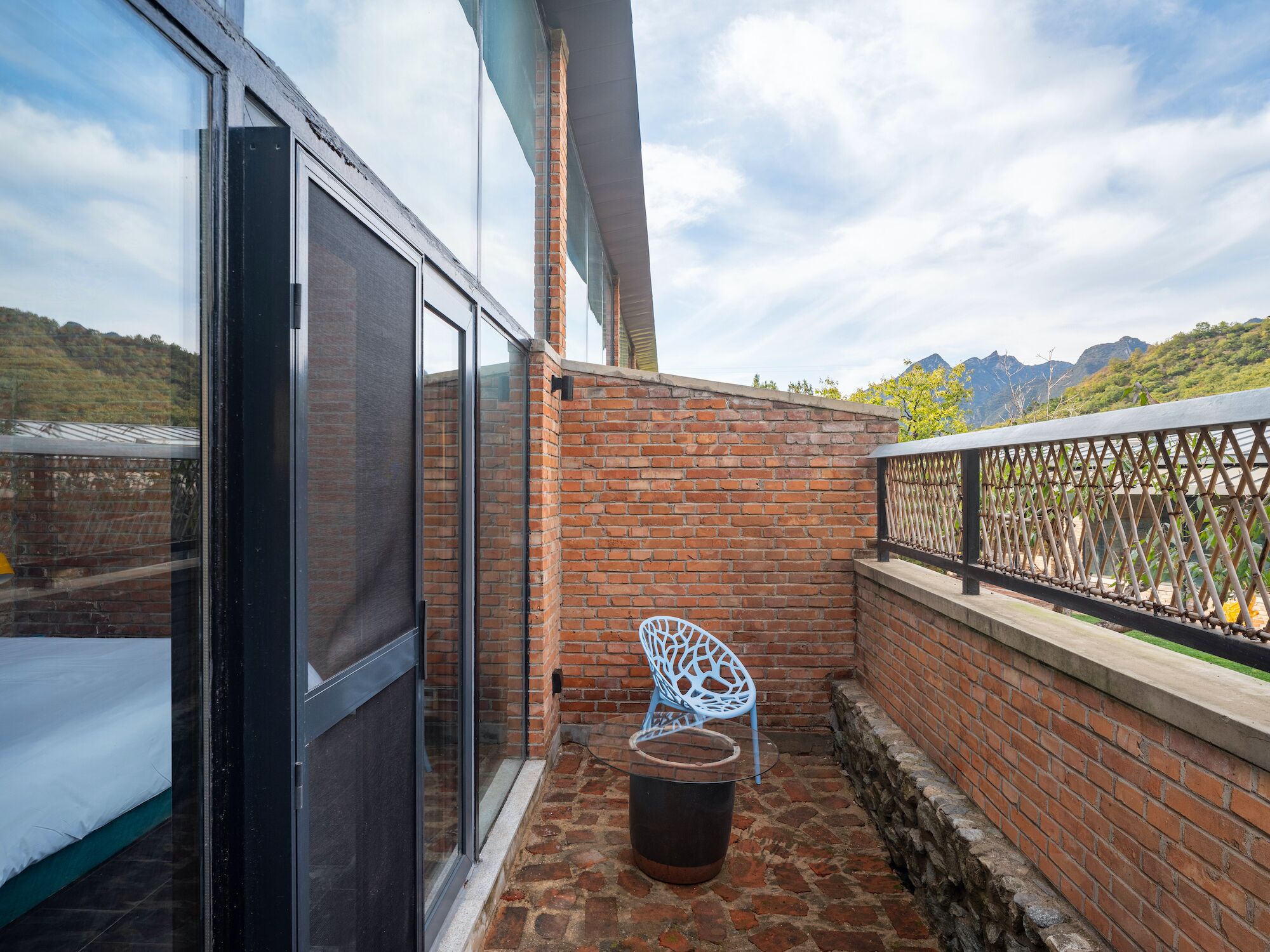 A balcony with a brick wall, a metal railing, and a blue chair.