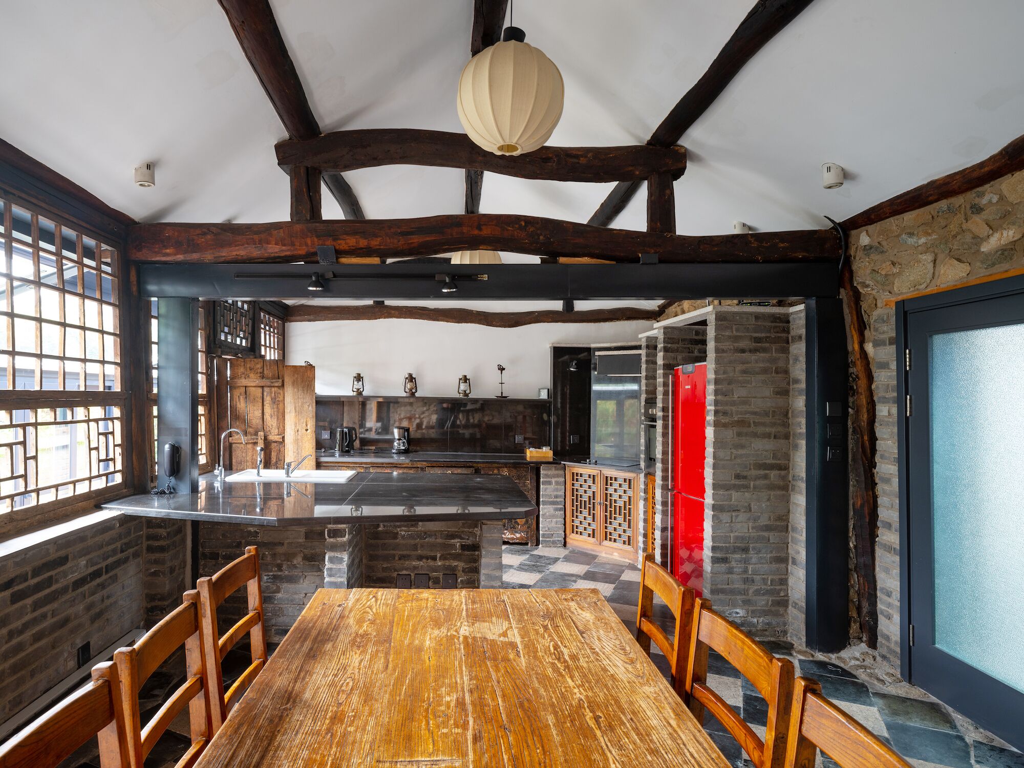 A spacious dining area with a wooden table and chairs, a kitchen with a red refrigerator, and a large window with a view.