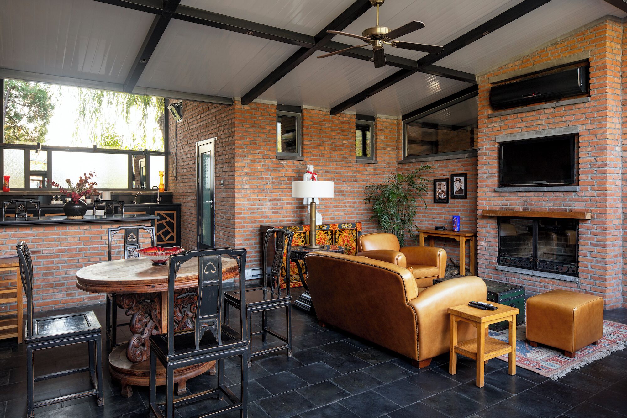 Een moderne woonkamer met een open haard van baksteen, leren banken en een eethoek met een tafel en stoelen.