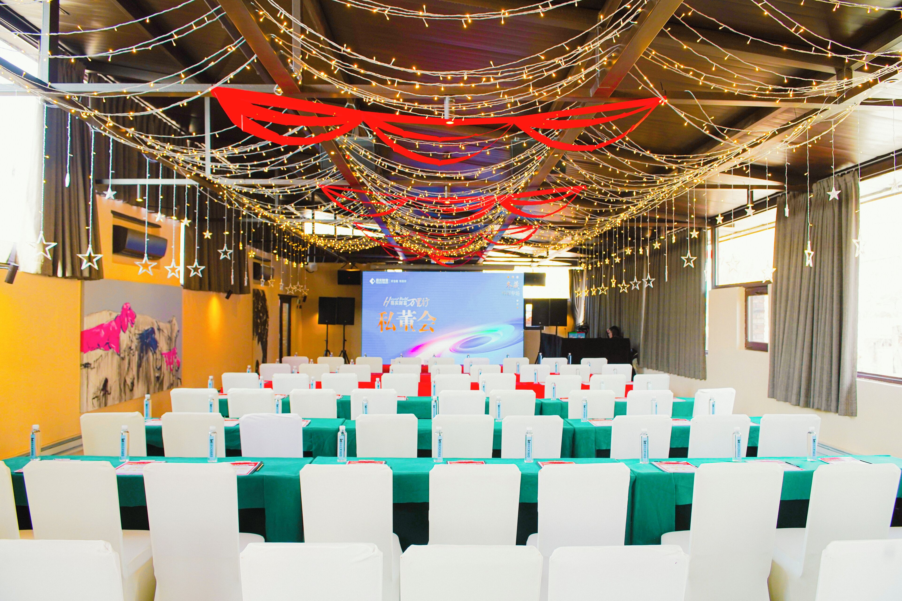 A conference room with rows of white chairs, green tablecloths, and a presentation screen.