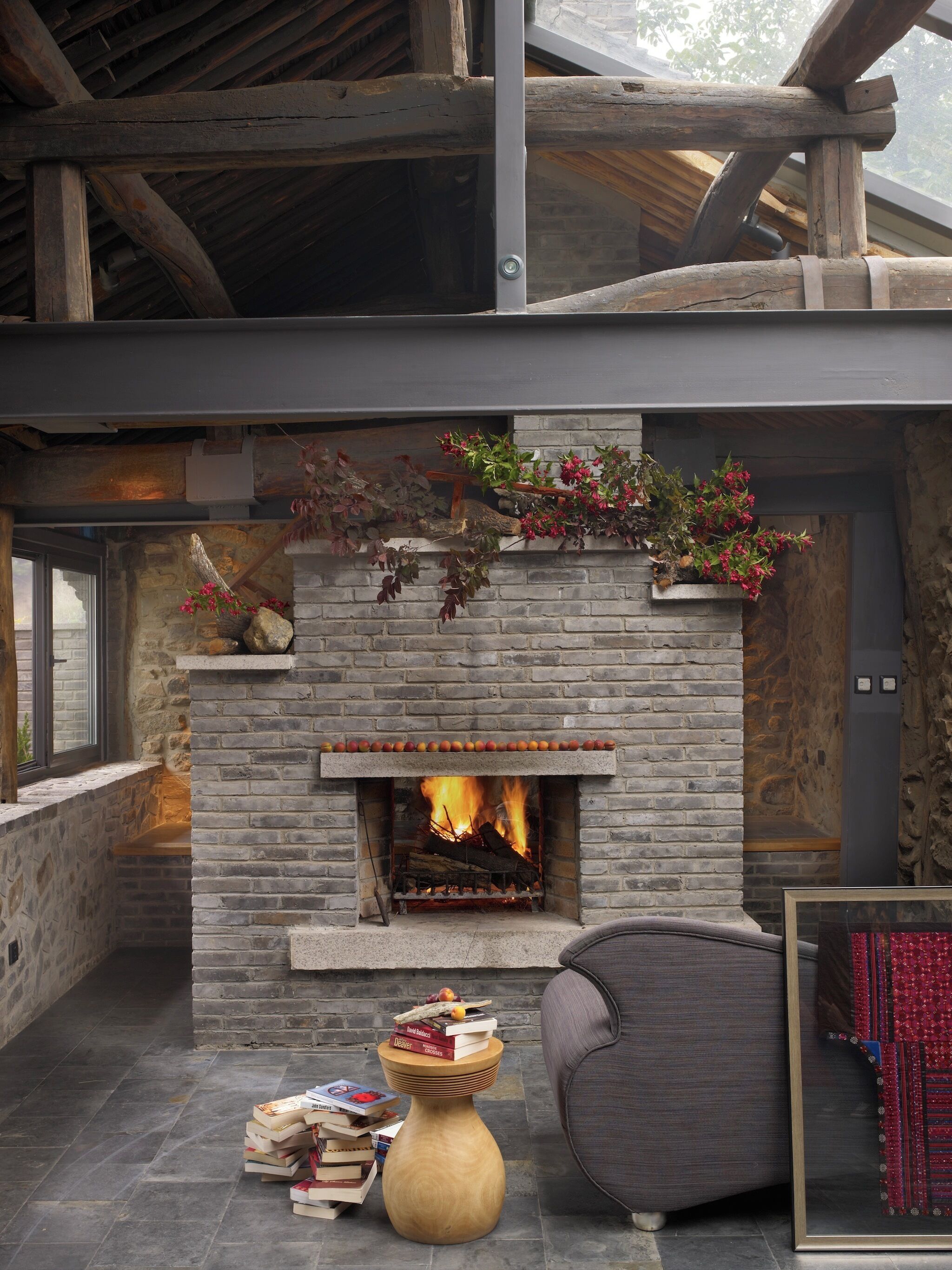 A stone fireplace with a fire, surrounded by books and a chair.