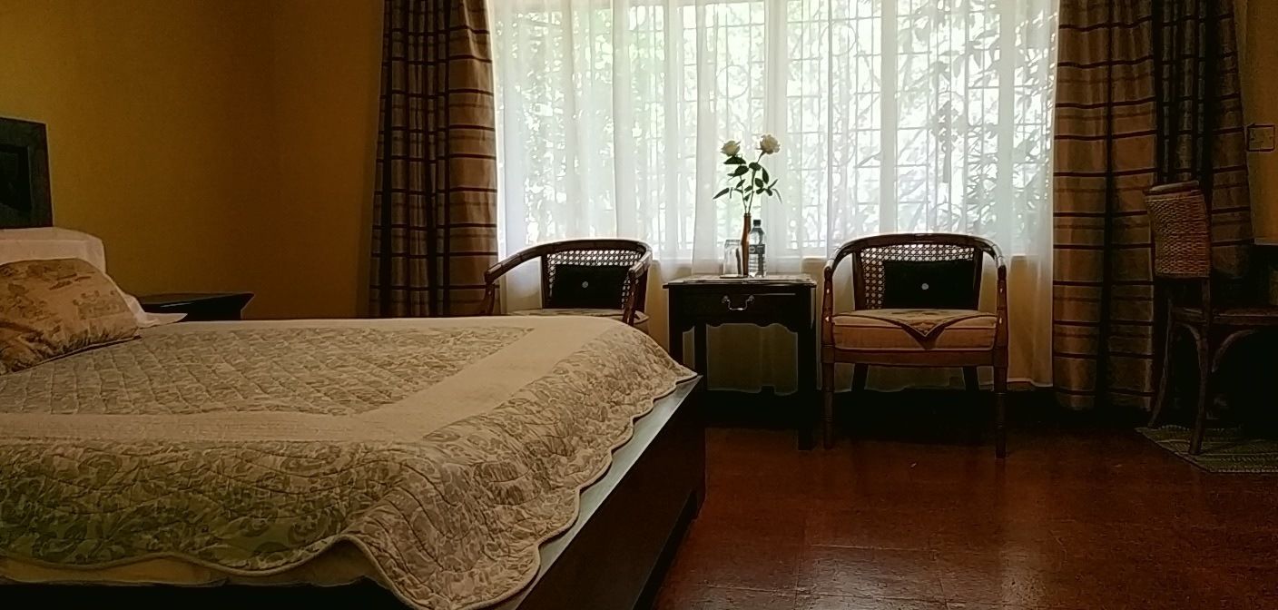 A bedroom with a large bed, two chairs, a nightstand, and a window with curtains.