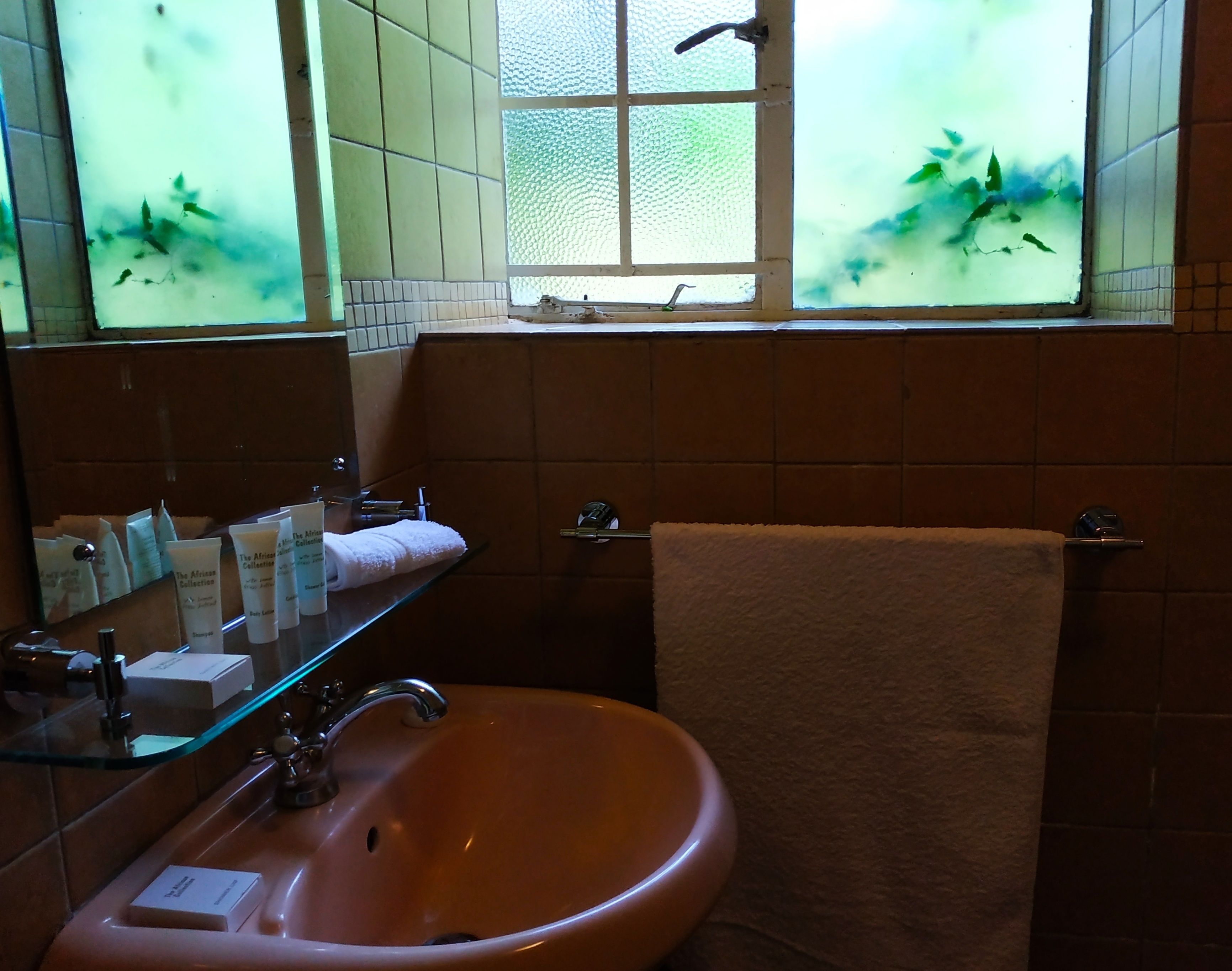 A bathroom with a glass shelf holding toiletries, a sink, and a towel rack.