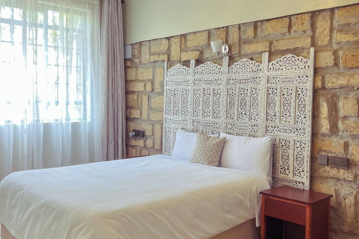 Quarto com cama grande, mesa de cabeceira, cabeceira decorativa e luminária pendente.