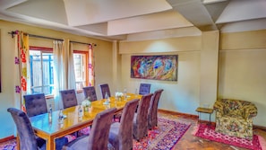 A conference room with a long table, multiple chairs, a floral-patterned armchair, a colorful abstract painting, and a patterned rug. - Zereniti House (Limuru)