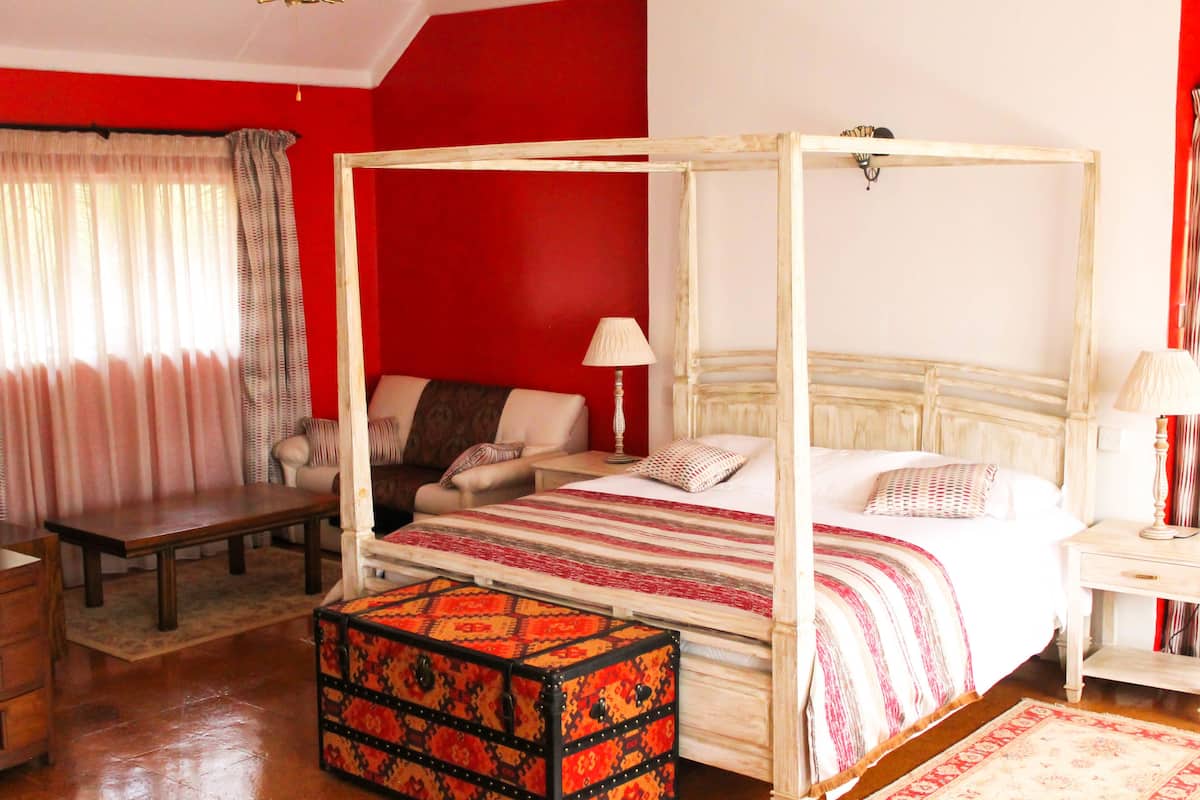 Uma cama de dossel com estrutura de madeira, uma mesa de cabeceira com luminária, um banco e um banquinho estampado.