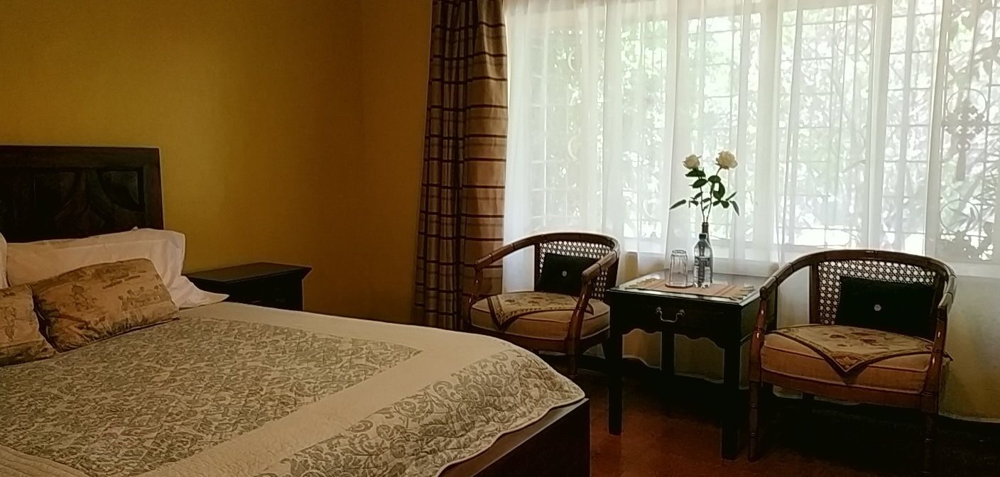 Een slaapkamer met een groot bed, twee stoelen, een kleine tafel en een raam met gordijnen.