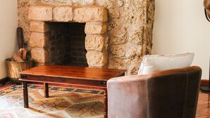 Um quarto aconchegante com lareira de pedra, uma mesa de madeira, um tapete estampado e uma poltrona de couro.