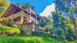 Um edifício com vários andares e varanda, cercado por vegetação exuberante e árvores.