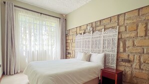 Quarto com cama grande, mesa de cabeceira, tapete estampado e parede de pedra com painéis decorativos.