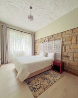 Un dormitorio con una cama grande, una mesita de noche, un tapete estampado y una pared de piedra con paneles decorativos.
