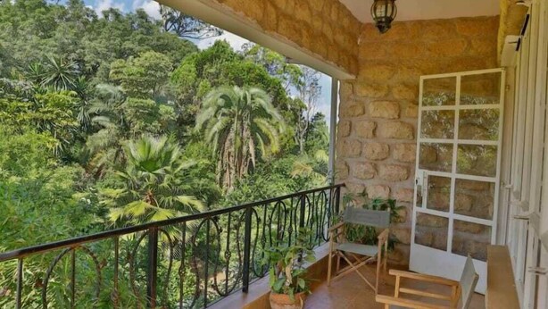 Varanda com parede de pedra, porta branca e vista para vegetação densa.