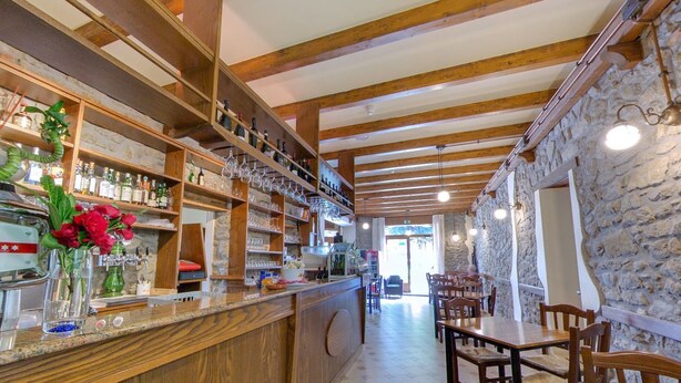 A bar area with wooden beams, stone walls, and shelves stocked with bottles and glasses. - Hotel Belvedere (Savignano sul Panaro)