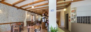 A rustic interior with stone walls, wooden beams, a central dining table, and a reception area with a counter and shelves.