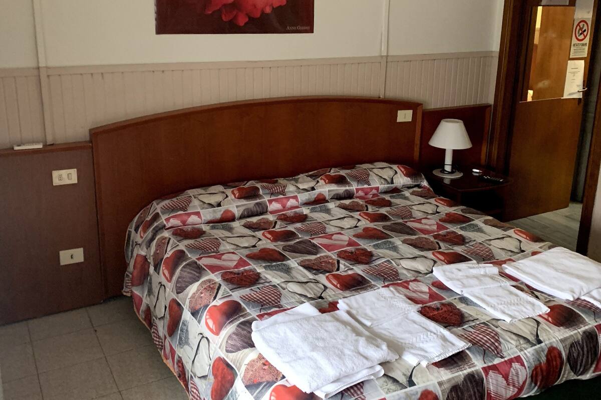 Hotellihuone, jossa on suuri sänky, yöpöytä, lamppu ja taulu seinällä.