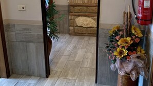 A hallway with a tiled floor, a potted plant, a decorative wall, and a fire extinguisher. - Hotel Belvedere (Savignano sul Panaro)
