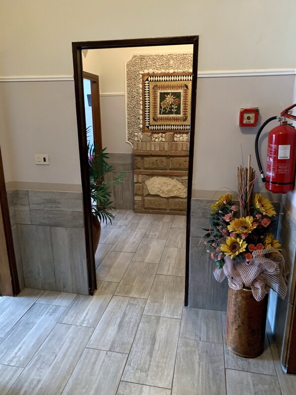 A hallway with a tiled floor, a potted plant, a decorative wall, and a fire extinguisher.