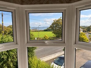 A window with a view of a road, greenery, and a clear sky. - The Anchorage Hotel (Holyhead)