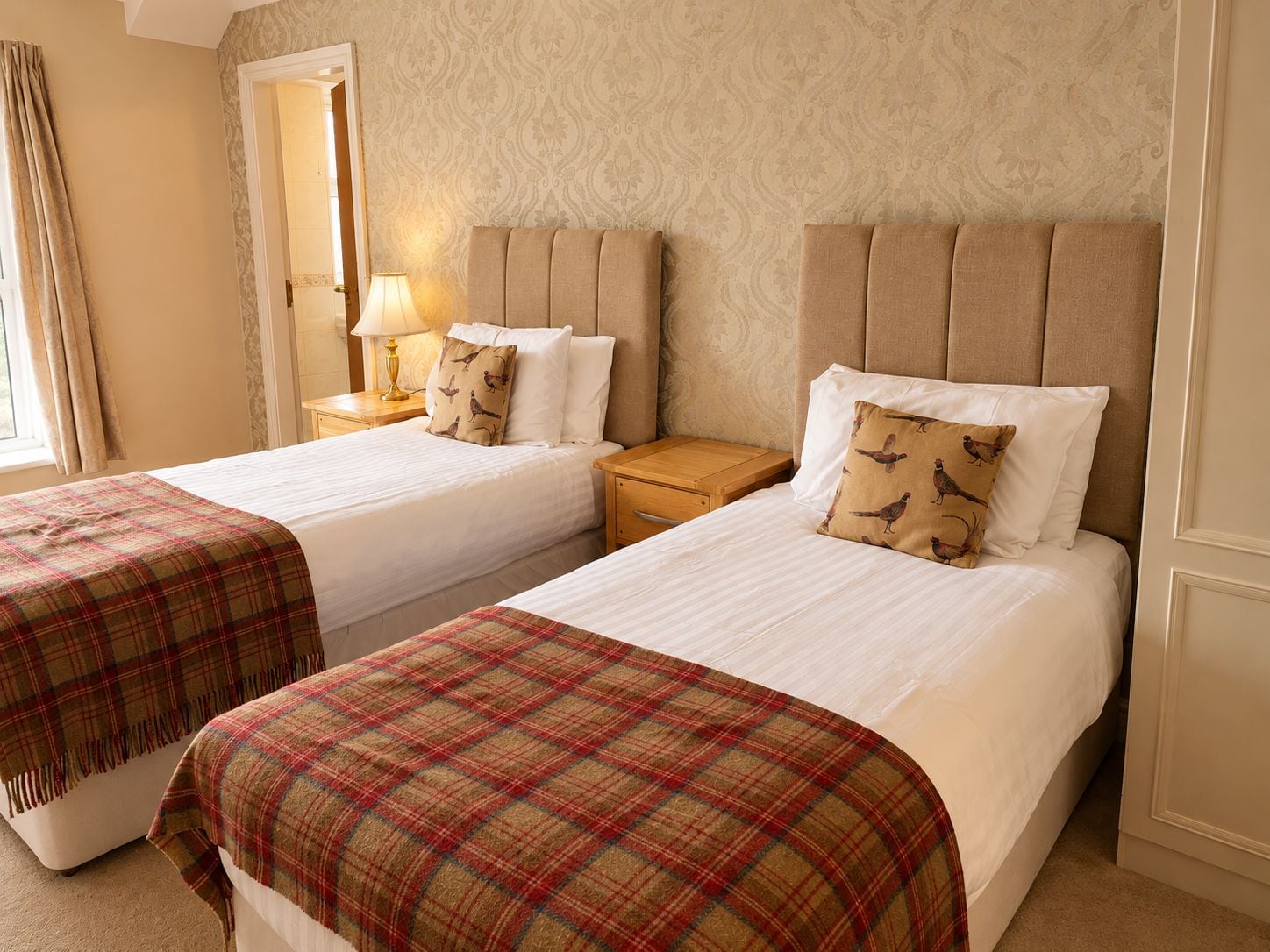 A hotel room with two beds, a nightstand with a lamp, and a window with curtains.
