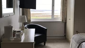 A hotel room with a bed, a desk with a lamp, a chair, a TV mounted on the wall, a wardrobe, and a window with a view of the landscape.