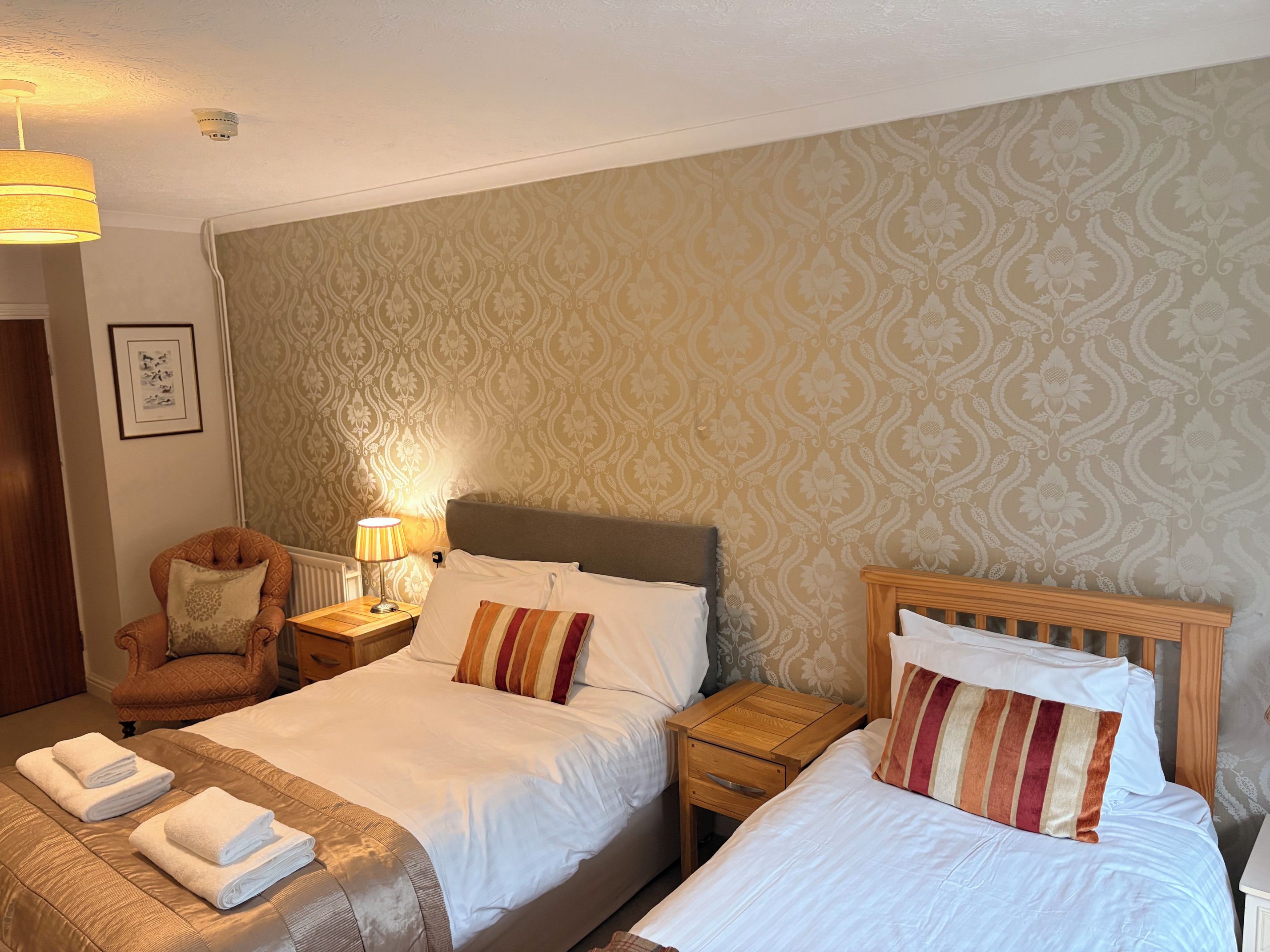 A hotel room with a bed, a chair, a nightstand, and a lamp.