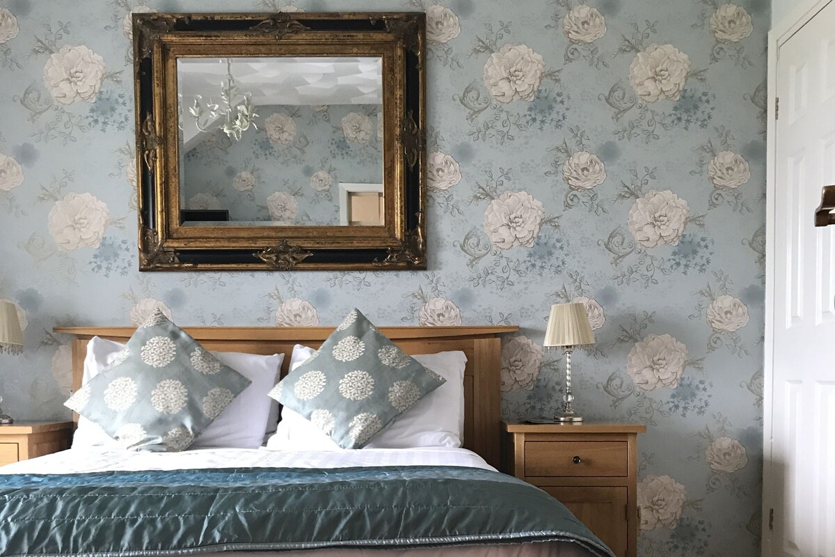 Une chambre à coucher avec un lit en bois, un papier peint à motifs floraux, un miroir et des lampes de chevet.
