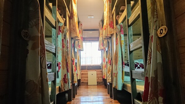 A corridor with bunk beds, each with a curtain. A window at the end allows natural light to enter.