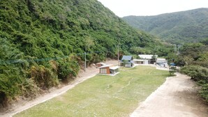 A rural property with a large grassy area, a dirt path, and several buildings including a main house and smaller structures.