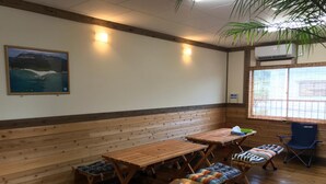 A room with wooden benches, tables, and a chair. There is a painting on the wall and an air conditioning unit near the window.