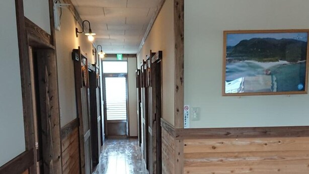 A hallway with wooden walls and floors, leading to a room with a painting of a landscape.