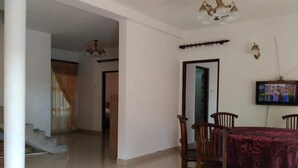 A dining area with a table and chairs, a chandelier, and a television on the wall. - The Fern Inn (Nuwara Eliya)