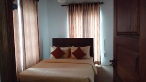 A bedroom with a bed, curtains, and a wooden door. - The Fern Inn (Nuwara Eliya)