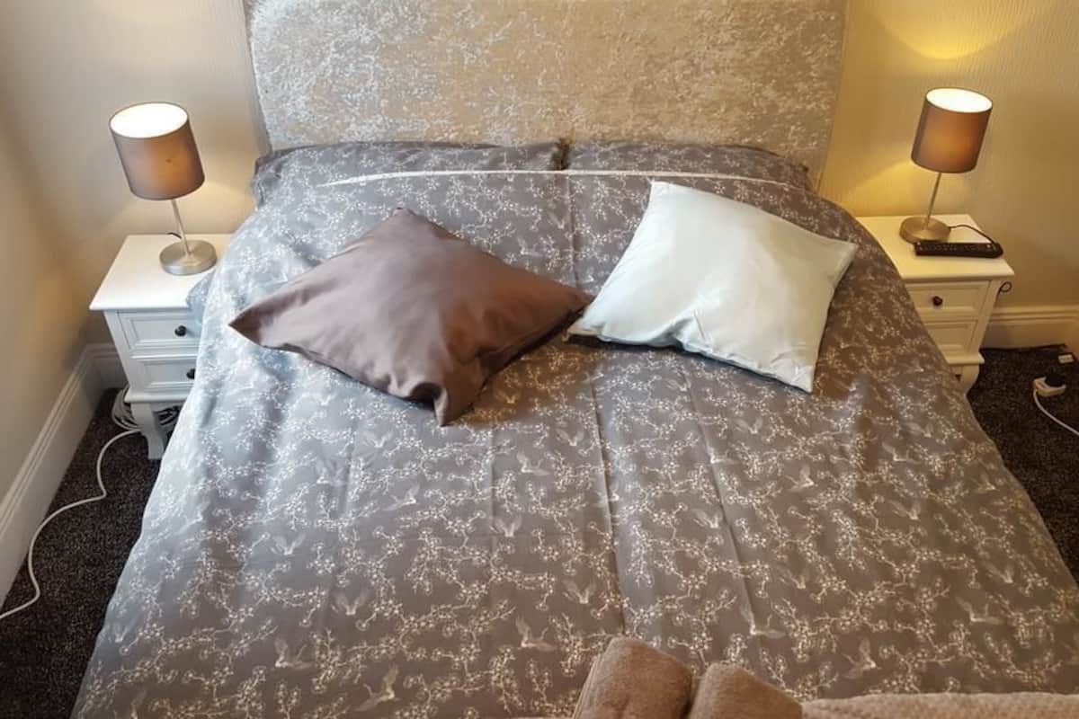 Uma cama bem arrumada com colcha estampada, duas luminárias de cabeceira e uma pequena mesa de cabeceira com abajur.
