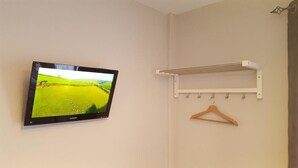 Une pièce avec un téléviseur fixé au mur qui diffuse un paysage, un étendoir blanc avec un cintre en bois, et un interrupteur sur le mur.