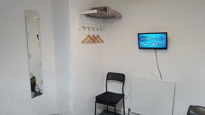 Une pièce avec une chaise noire, un miroir, un radiateur, un téléviseur fixé au mur et un étendoir à linge.