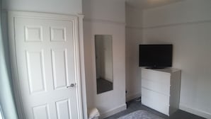 A room with a white door, a white dresser, a flat-screen TV on top, and a mirror on the wall. - Alexandra Park Guest House (Belfast)